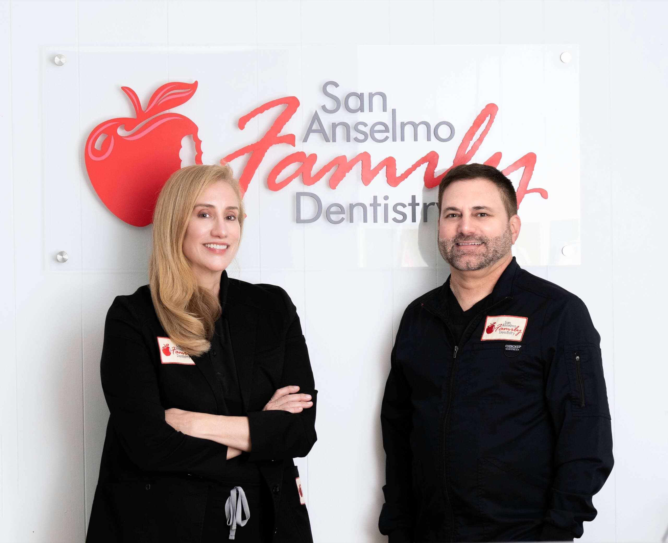 Dr. Rosemarie Goldstein and Dr. Anthony Costella, San Anselmo Family Dentistry team, stand in front of the practice logo.