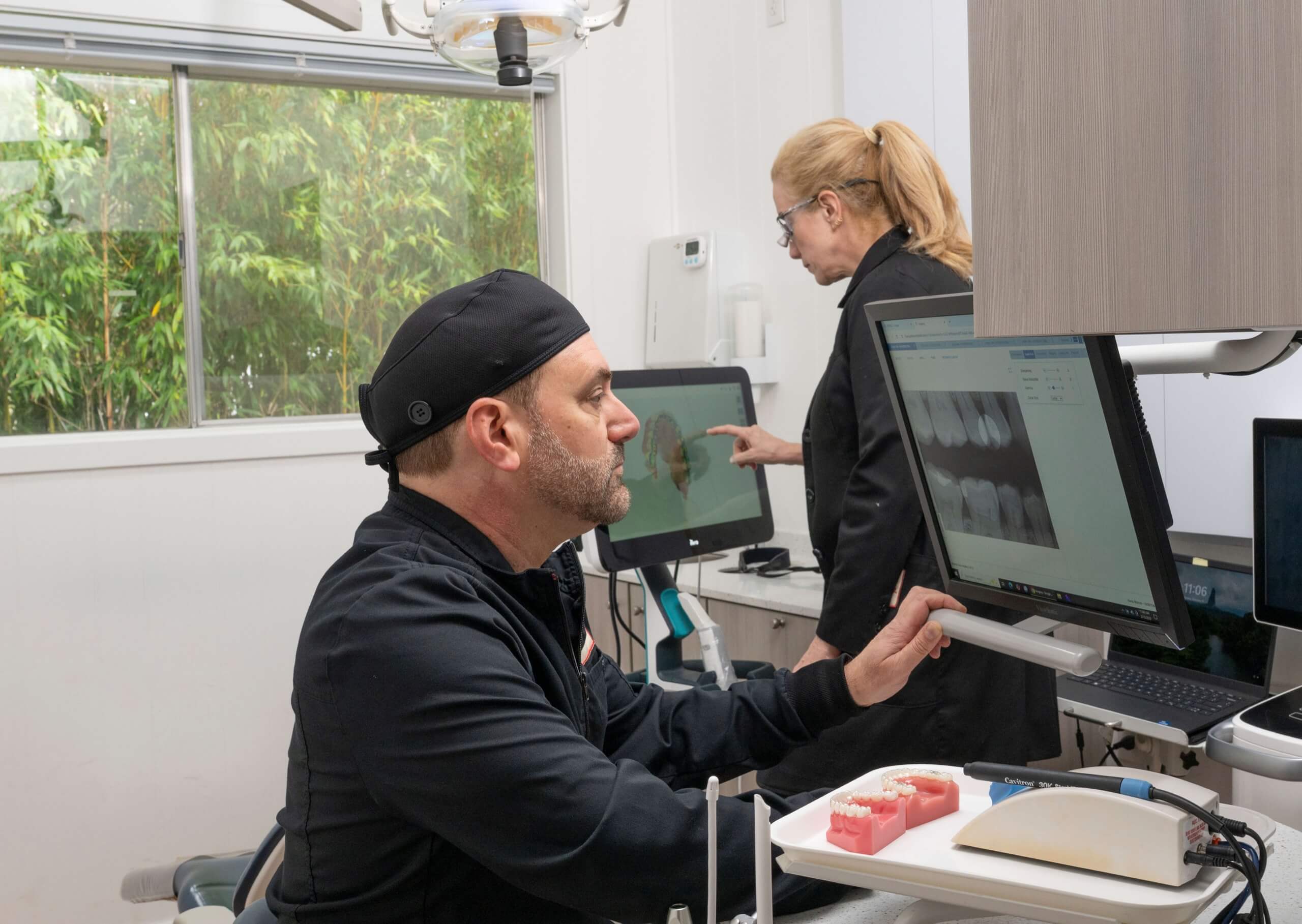 Dental professionals review digital X-rays and 3D scans on monitors in a modern treatment room, showcasing high-tech gentle dentistry.