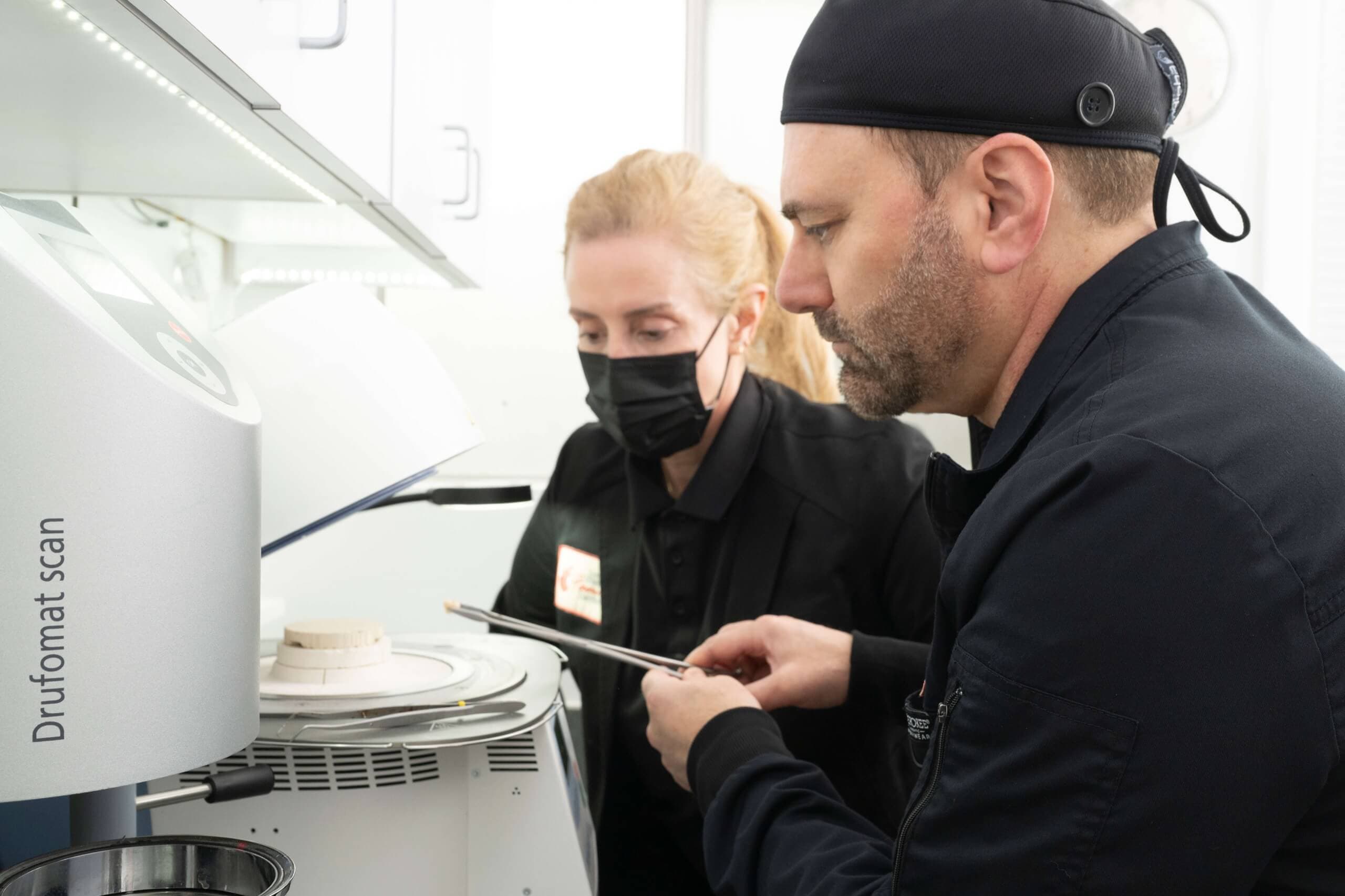 Two dental professionals, one masked, meticulously work with a high-tech Drufomat scan machine, demonstrating advanced dental technology.