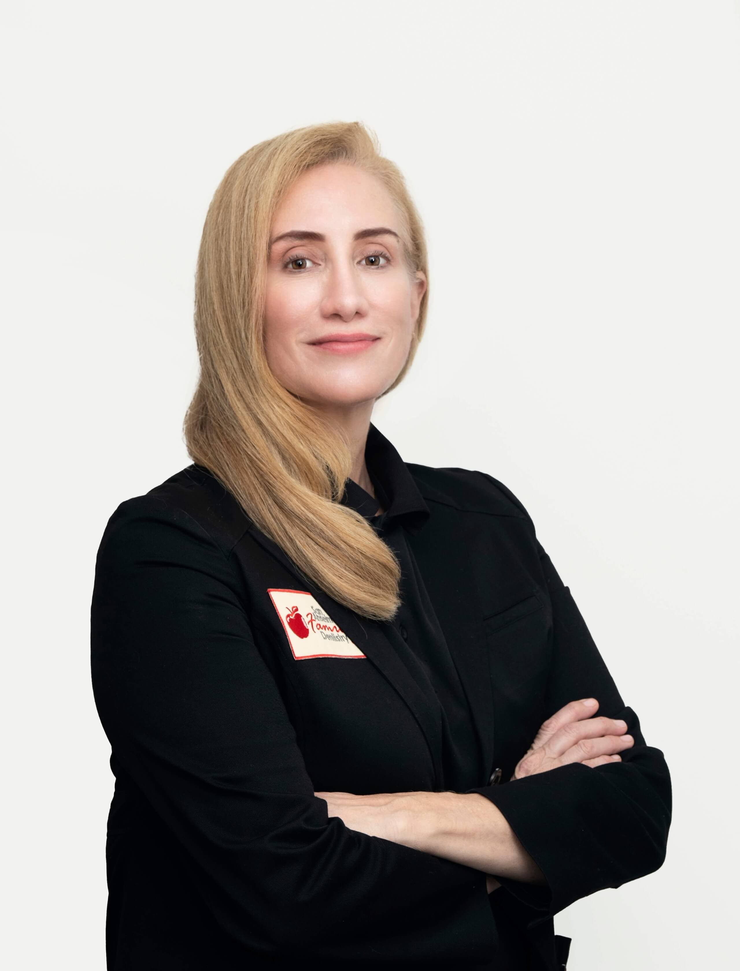 Dr. Rosemarie Goldstein in black blazer with San Anselmo Family Dentistry name tag, arms crossed, smiling gently at the camera.